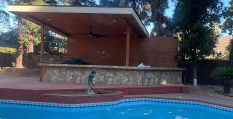 Modern poolside cabana with wooden roof structure overlooking a bright blue swimming pool with tiled edge