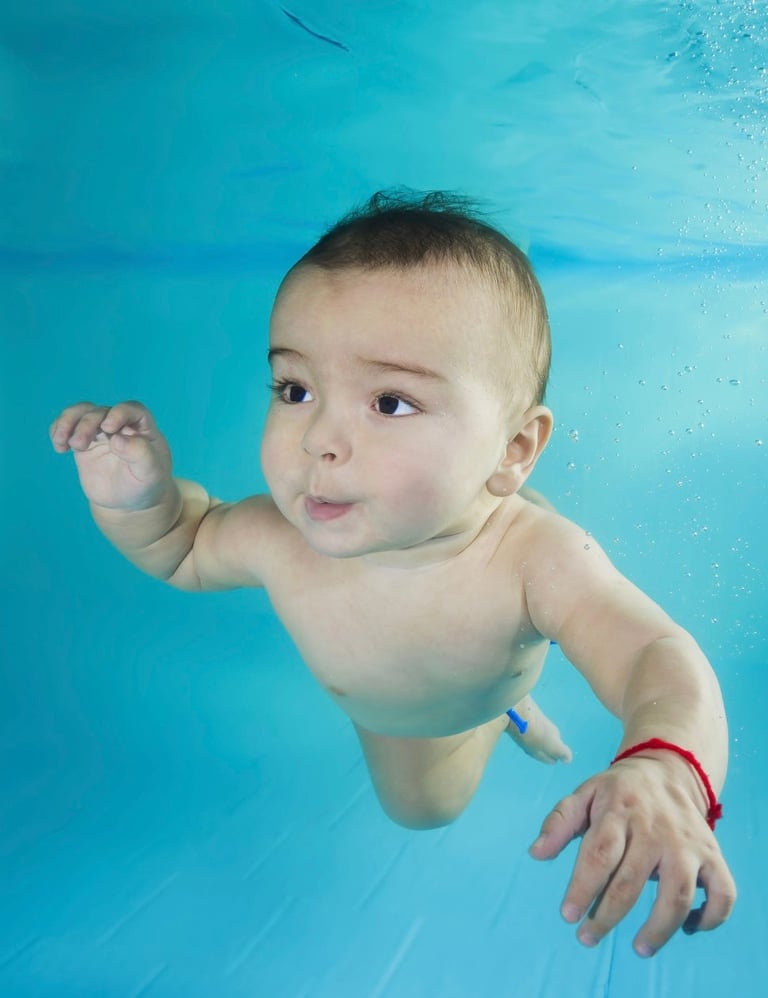 Baby swimming underwater in a pool with a bright blue background, wearing a red bracelet