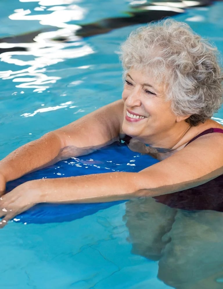 Senior woman with gray hair smiling while holding a blue kickboard in a swimming pool
