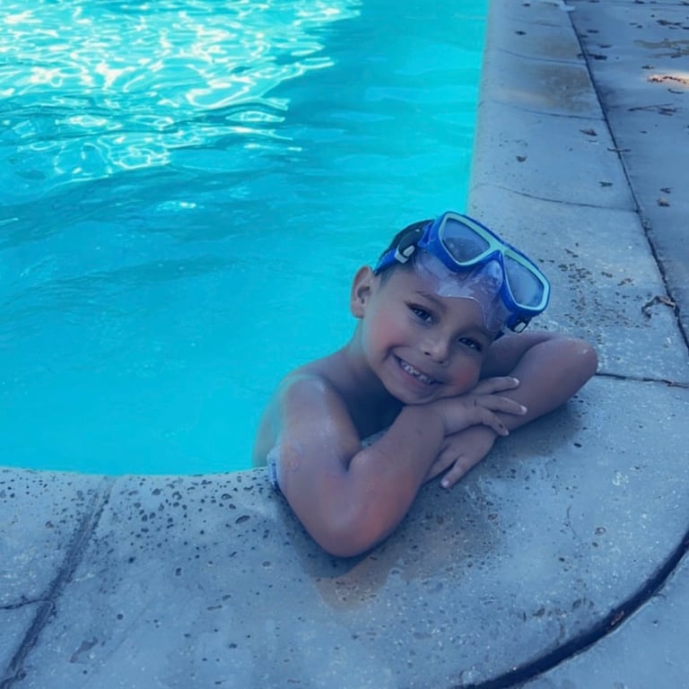 Young child wearing blue swim goggles smiling at the edge of a swimming pool